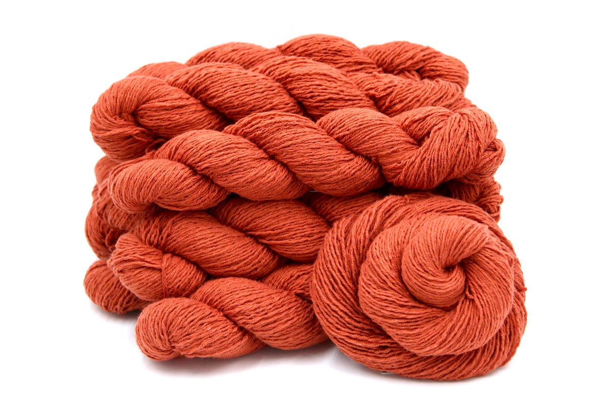 Several skeins of Vegan, Rusty Red/ Terracotta Orange, Cotton/ Acrylic, Fingering weight recycled by hand from unwanted sweaters stacked on top of each other attractively. 
