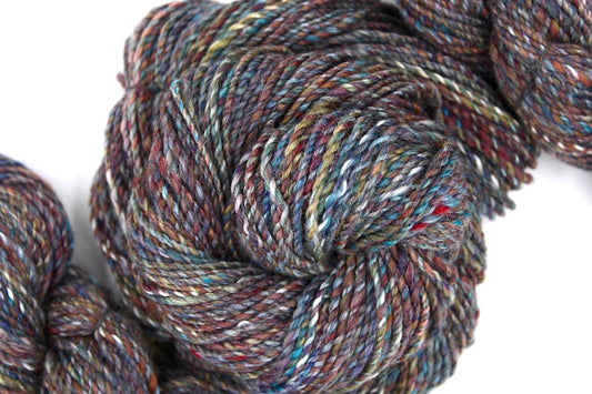 A one of a kind, hand dyed variegated skein of multicolored Maroon, Red, Grey, Blue, Yellow, and Brown self-striping wool Yarn coiled attractively in the center of the frame.