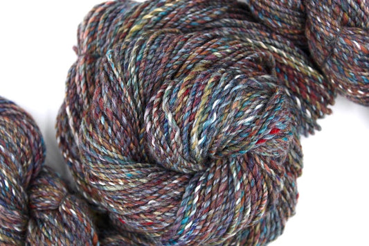 A one of a kind, hand dyed variegated skein of multicolored Maroon, Red, Grey, Blue, Yellow, and Brown self-striping wool Yarn coiled attractively in the center of the frame. 
