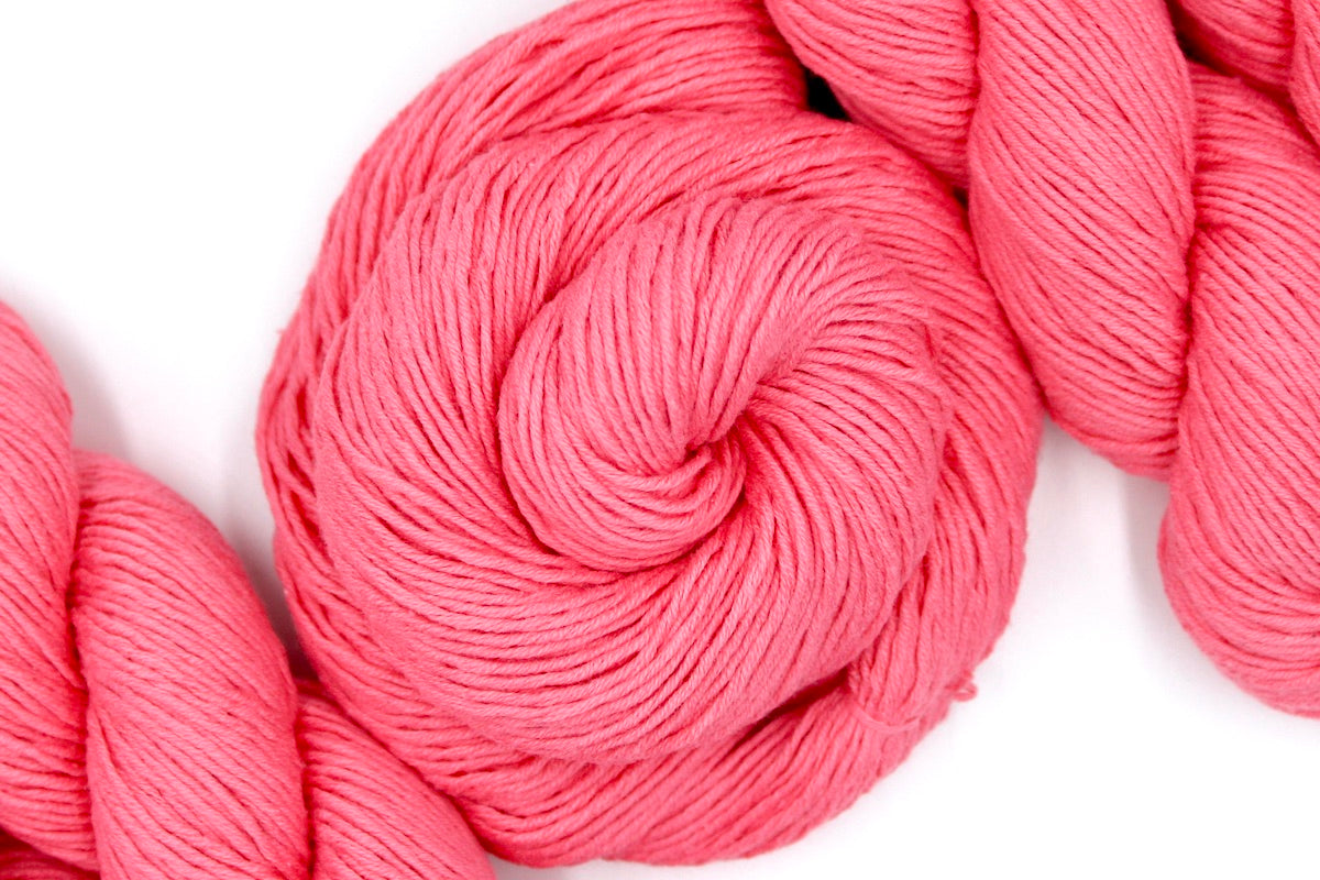 A skein of Vegan, Neon Rose Pink/ Fuchsia, 100% Cotton, Sport weight Yarn recycled by hand from unwanted sweaters swirled attractively in the center of the frame. 