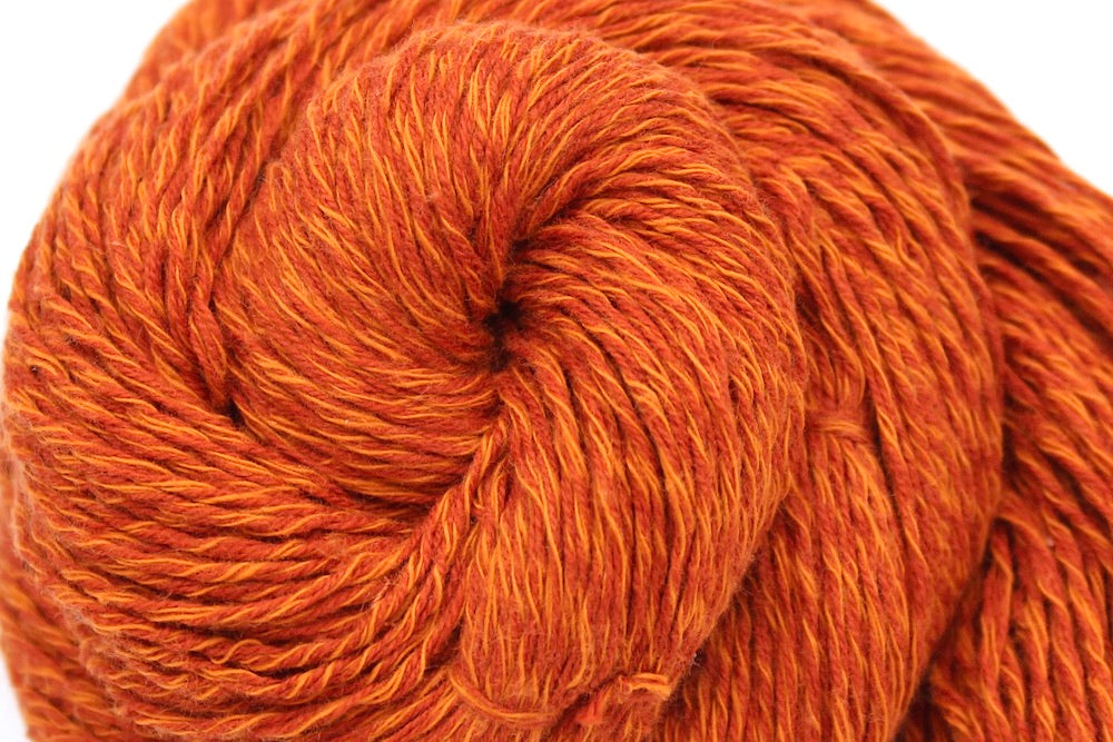 A close up shot of a skein of Vegan, Bright Rusty Red/ Turmeric Orange, 100% Cotton, Sport weight Yarn recycled by hand from unwanted sweaters beautifully coiled in the center of the frame. 