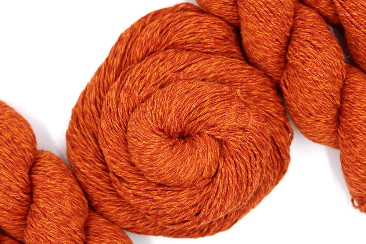 A skein of Vegan, Bright Rusty Red/ Turmeric Orange, 100% Cotton, Sport weight Yarn recycled by hand from unwanted sweaters swirled attractively in the center of the frame. 