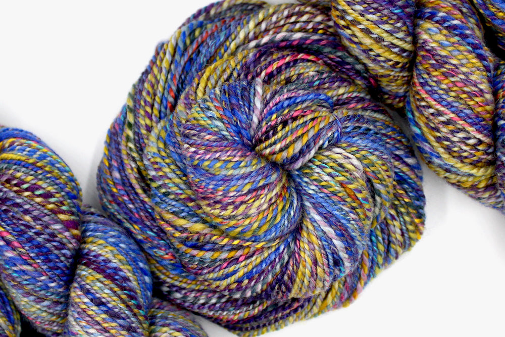 A one of a kind Worsted Weight, hand dyed variegated skein of Rainbow multicolored self-striping Hand spun Yarn, made with Hand Dyed Wool and Bamboo; coiled attractively in the center of the frame. 