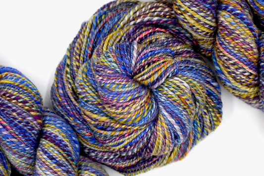 A one of a kind Worsted Weight, hand dyed variegated skein of Rainbow multicolored self-striping Hand spun Yarn, made with Hand Dyed Wool and Bamboo; coiled attractively in the center of the frame. 