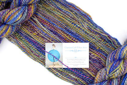A one of a kind, Worsted Weight, hand dyed variegated skein of Rainbow multicolored self-striping Hand spun Yarn, made with Hand Dyed Wool and Bamboo, draped diagonally across the frame, so you can really see the color play. 