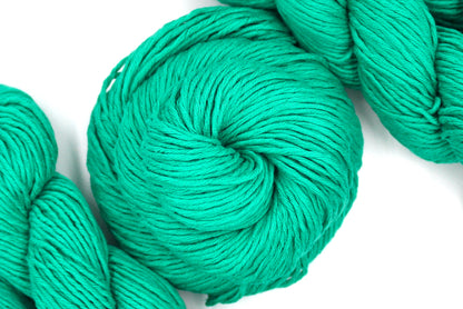 A skein of Vegan, Bright Blue Green, 100% Cotton, Worsted Weight Yarn recycled by hand from unwanted sweaters swirled attractively in the center of the frame. 