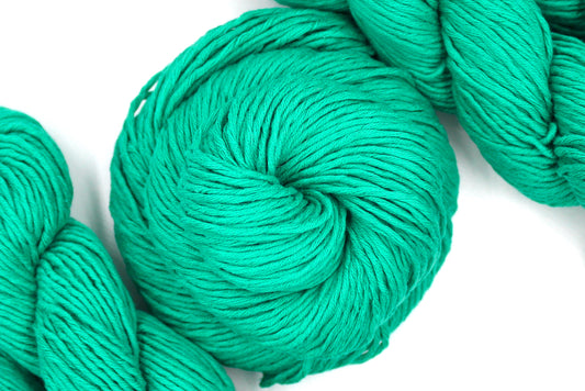 A skein of Vegan, Bright Blue Green, 100% Cotton, Worsted Weight Yarn recycled by hand from unwanted sweaters swirled attractively in the center of the frame. 