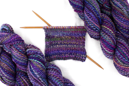 A sample swatch knitted from a one of a kind, Worsted weight, hand dyed variegated skein of multicolored Purple, Fuchsia, Green, Navy Blue, Teal, and Pink self-striping wool Yarn. 