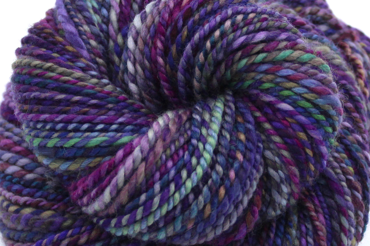 A close up view of a one of a kind, Worsted Weight, hand dyed variegated skein of multicolored Purple, Fuchsia, Green, Navy Blue, Teal, and Pink self-striping wool Yarn. 