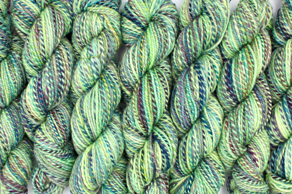 Six one of a kind, Worsted Weight, hand dyed variegated skein of multicolored Lime Green, Yellow, Seafoam, Navy, Blue, and Purple self-striping 100% Superwash Merino wool Yarn lined up side by side. 