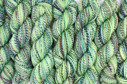 Six one of a kind, Worsted Weight, hand dyed variegated skein of multicolored Lime Green, Yellow, Seafoam, Navy, Blue, and Purple self-striping 100% Superwash Merino wool Yarn lined up side by side. 