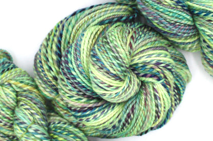 A one of a kind, Worsted Weight, hand dyed variegated skein of multicolored Lime Green, Yellow, Seafoam, Navy, Blue, and Purple self-striping 100% Superwash Merino wool Yarn coiled attractively in the center of the frame. 