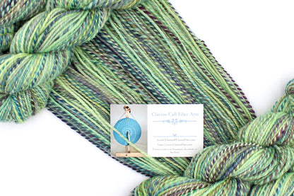 A one of a kind, Worsted Weight, hand dyed variegated skein of multicolored Lime Green, Yellow, Seafoam, Navy, Blue, and Purple self-striping 100% Superwash Merino wool Yarn draped diagonally across the frame, so you can really see the color play. 