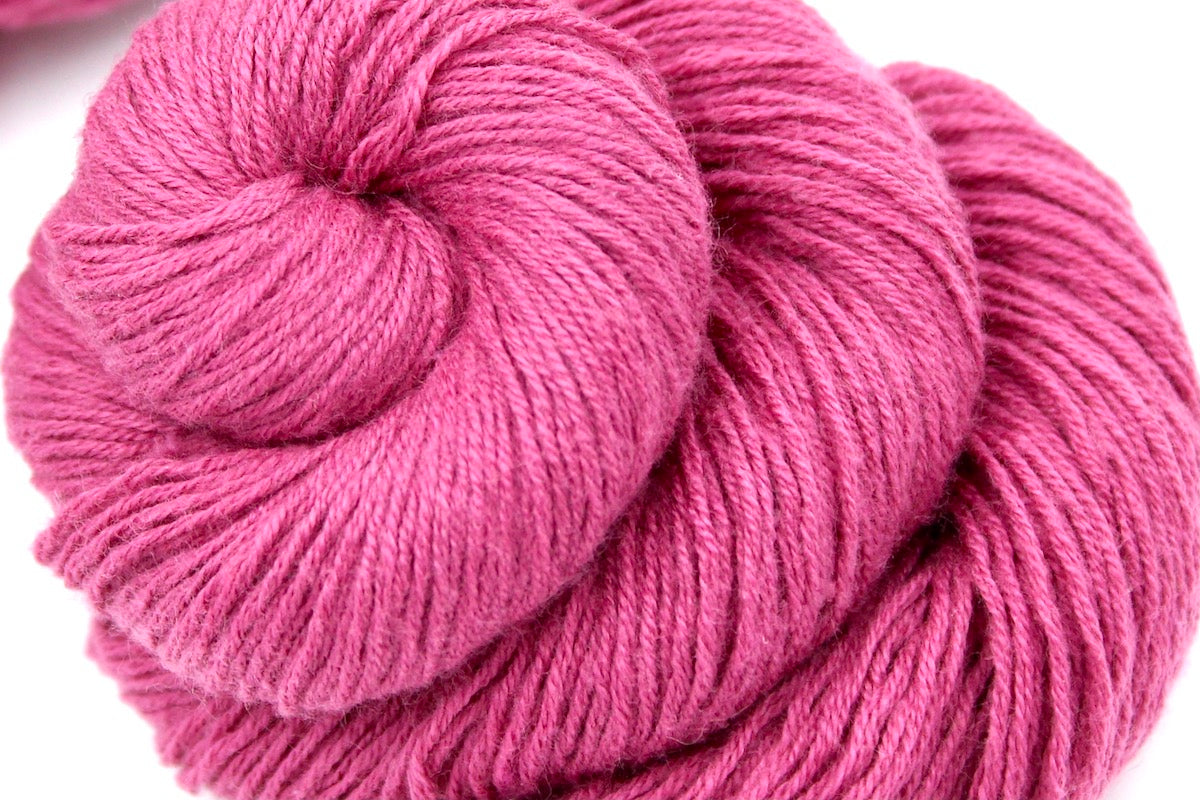 A close up shot of a skein of Vegan, Watermelon Fuchsia/ Rose Pink, Cotton/ Rayon/ Nylon, Fingering weight Yarn recycled by hand from unwanted sweaters beautifully coiled in the center of the frame. 