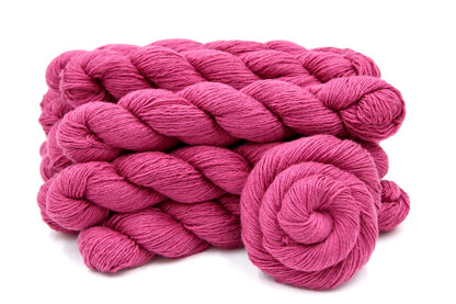 Several skeins of Vegan, Watermelon Fuchsia/ Rose Pink, Cotton/ Rayon/ Nylon, Fingering weight recycled by hand from unwanted sweaters stacked on top of each other attractively. 