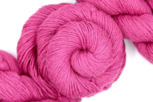 A skein of Vegan, Watermelon Fuchsia/ Rose Pink, Cotton/ Rayon/ Nylon, Fingering weight Yarn recycled by hand from unwanted sweaters swirled attractively in the center of the frame. 