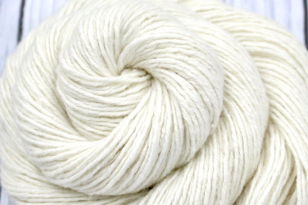 A close up shot of a skein of Cream/ Off White/ Ecru/ Pearl, Rayon/ Wool/ Cotton/ Nylon/ Rabbit Hair, Sport weight Yarn recycled by hand from unwanted sweaters beautifully coiled in the center of the frame. 