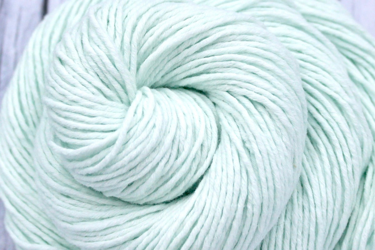 A close up shot of a skein of Vegan, Light Pastel Mint Green, 100% Cotton, Sport weight Yarn recycled by hand from unwanted sweaters beautifully coiled in the center of the frame. 