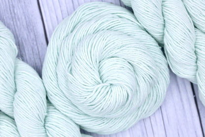 A skein of Vegan, Light Pastel Mint Green, 100% Cotton, Sport weight Yarn recycled by hand from unwanted sweaters swirled attractively in the center of the frame. 