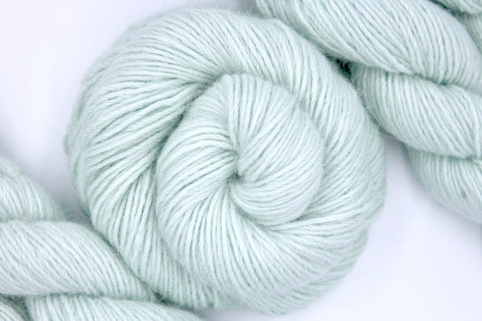A skein of Light Pastel Mint Green, Nylon/ Angora, Dk weight Yarn recycled by hand from unwanted sweaters swirled attractively in the center of the frame. 