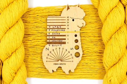 A skein of Vegan, Mustard Yellow, 100% Cotton, Sport Weight Yarn recycled by hand from unwanted sweaters draped over the center of the frame with one strand on top of a Llama shaped Yarn weight tool, to better illustrate the thickness of the yarn. 