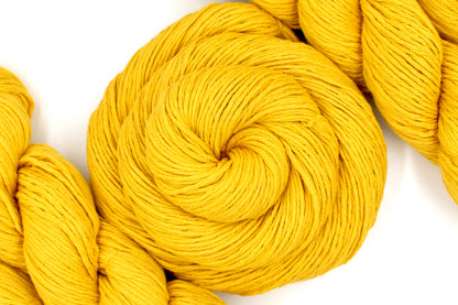 A skein of Vegan, Mustard Yellow, 100% Cotton, Sport Weight Yarn recycled by hand from unwanted sweaters swirled attractively in the center of the frame. 