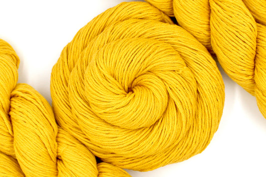 A skein of Vegan, Mustard Yellow, 100% Cotton, Sport Weight Yarn recycled by hand from unwanted sweaters swirled attractively in the center of the frame. 